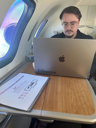 Man working on a laptop inside a private jet, with documents on the table.